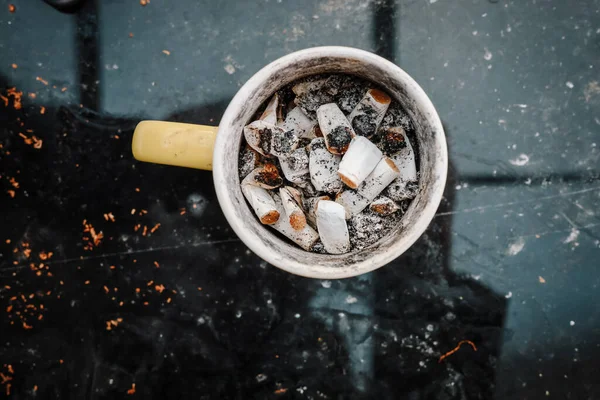 Ashtray, coffee cup as an ashtray filled with cigarette butts, photographed from above, focus on the butts.