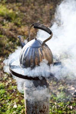 Su dolu metal bir çaydanlık bahçedeki yanan odun sobasında, su kaynıyor..