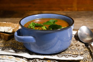 Ahşap bir yemek masasında, peçetenin üzerinde mavi bir seramik kasede mantar çorbası. Ev yemeği.