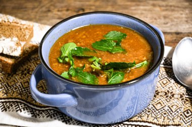 Ahşap bir yemek masasında, peçetenin üzerinde mavi bir seramik kasede mantar çorbası. Ev yemeği.