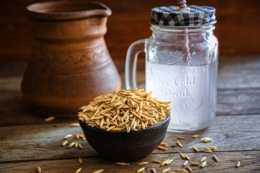 On the wooden kitchen table are a ceramic bowl of oat grains, a glass cup with oat kvass on a kitchen napkin, and an earthen jug. Village life.