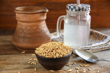 On the wooden kitchen table are a ceramic bowl of oat grains, a glass cup with oat kvass on a kitchen napkin, and an earthen jug. Village life.