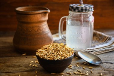 On the wooden kitchen table are a ceramic bowl of oat grains, a glass cup with oat kvass on a kitchen napkin, and an earthen jug. Village life.