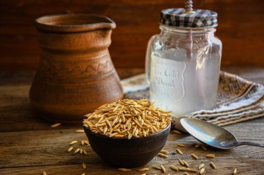 On the wooden kitchen table are a ceramic bowl of oat grains, a glass cup with oat kvass on a kitchen napkin, and an earthen jug. Village life.