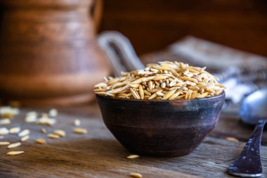 On the wooden kitchen table are a ceramic bowl of oat grains, a glass cup with oat kvass on a kitchen napkin, and an earthen jug. Village life.