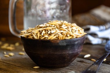 On the wooden kitchen table are a ceramic bowl of oat grains, a glass cup with oat kvass on a kitchen napkin, and an earthen jug. Village life.