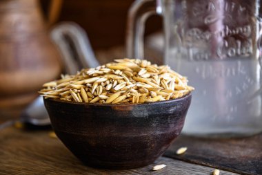On the wooden kitchen table are a ceramic bowl of oat grains, a glass cup with oat kvass on a kitchen napkin, and an earthen jug. Village life.