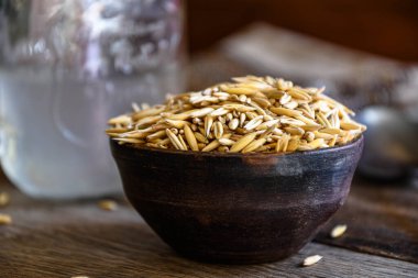 On the wooden kitchen table are a ceramic bowl of oat grains, a glass cup with oat kvass on a kitchen napkin, and an earthen jug. Village life.