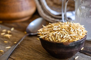 On the wooden kitchen table are a ceramic bowl of oat grains, a glass cup with oat kvass on a kitchen napkin, and an earthen jug. Village life.