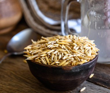 On the wooden kitchen table are a ceramic bowl of oat grains, a glass cup with oat kvass on a kitchen napkin, and an earthen jug. Village life.