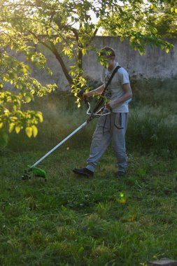 Adam çim biçiyor, kesiyor, fazla büyümüş bir bahçede çim biçiyor bahçe biçme makinesi ya da moto-tırpan kesiyor. Bahçe temizliği, bahçe temizliği. Umurumuzda değil....