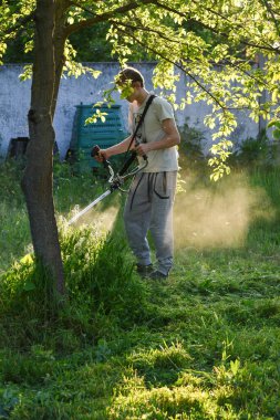 Adam çim biçiyor, kesiyor, fazla büyümüş bir bahçede çim biçiyor bahçe biçme makinesi ya da moto-tırpan kesiyor. Bahçe temizliği, bahçe temizliği. Umurumuzda değil....