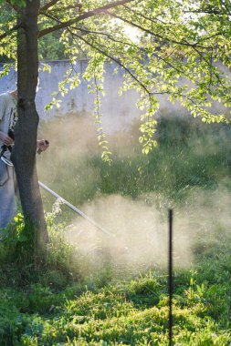 Adam çim biçiyor, kesiyor, fazla büyümüş bir bahçede çim biçiyor bahçe biçme makinesi ya da moto-tırpan kesiyor. Bahçe temizliği, bahçe temizliği. Umurumuzda değil....