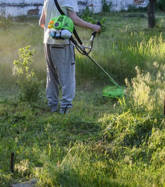 Adam çim biçiyor, kesiyor, fazla büyümüş bir bahçede çim biçiyor bahçe biçme makinesi ya da moto-tırpan kesiyor. Bahçe temizliği, bahçe temizliği. Umurumuzda değil....