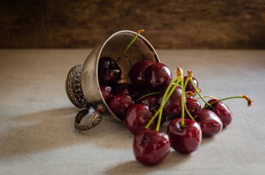 Masanın üzerinde olgun kirazlı gümüş bir kupa var..
