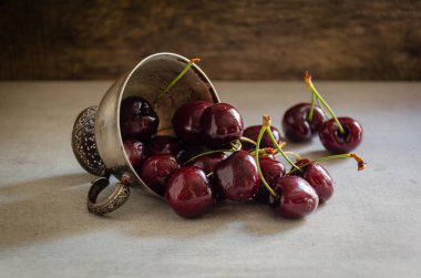 Masanın üzerinde olgun kirazlı gümüş bir kupa var..