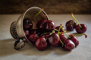Masanın üzerinde olgun kirazlı gümüş bir kupa var..