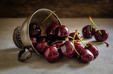 Masanın üzerinde olgun kirazlı gümüş bir kupa var..