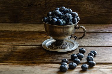 Blueberries in a silver cup, on a wooden table. Ripe berries in the kitchen, harvest.