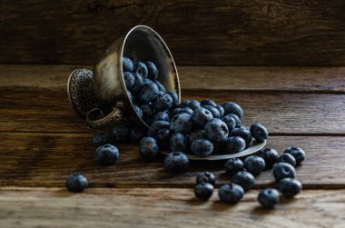 Blueberries are scattered from a silver cup, on a wooden table. Ripe berries in the kitchen, harvest.