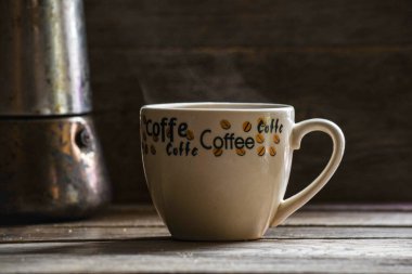 A cup of black coffee and a geyser on a wooden table.