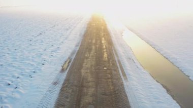 Buzlu ve karlı bir yolda, ufukta güzel bir günbatımı ve buzdan yansıyan korkunç bir ışık ve balık havuzunun yanında bir kamera dronu ile uçmak.