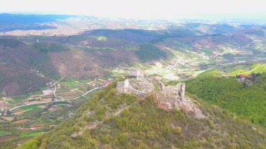 Dağın eteğinde vadisi olan bir tepenin tepesindeki ortaçağ kalesinin insansız hava görüntüsü.
