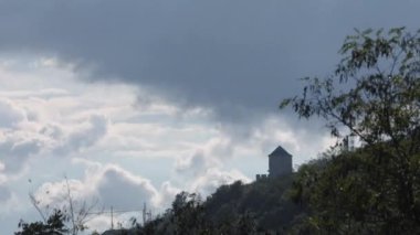 Vrsac Tepesi 'nin tepesinde, büyük bir ağacın gölgesinden geçen gri bulutlu bir ortaçağ takviyeli kulesinin zaman geçişi.