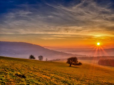 Gün batımında yalnız ağaçların olduğu manzaralı tepe manzarası vadiye bakan, yüksek bulutlu mavi gökyüzü, güneş. Sonbahar akşamı. Beyaz Karpatlar Dağları, Çek Cumhuriyeti.