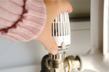 Kadın, beyaz radyatörde termostat, yakın çekim kadın eli, ısı tasarrufu kavramı, ısınma mevsiminin başlangıcı, sığ alan derinliği ile evdeki ısıyı düzenliyor.