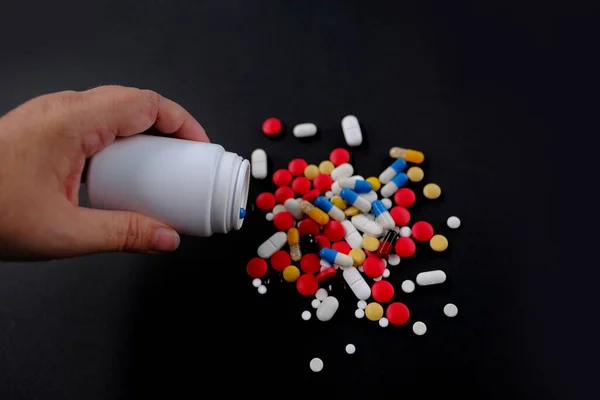 閉じられた女性の手は 多くの色の錠剤 黒の背景に白い瓶のカプセルを注ぐ 健康を維持する概念 薬物治療 ビタミン 薬物中毒 — ストック写真