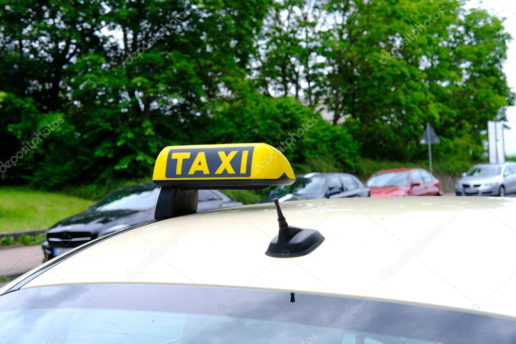 white passenger car with a yellow taxi sign on the roof at the top is waiting for its client, observes the rules of road, vehicles pass by, the concept of car services to population in city