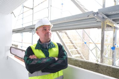 Erkek ustabaşı, beyaz şapkalı işçi, inşaat sahasında duruyor. Binaların, binaların, yapıların, iskelelerin tamiri kavramı...