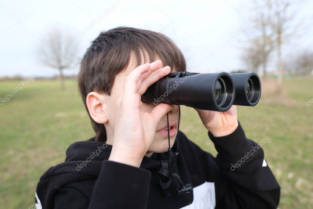 boy, guy 8-10 years old stalker looks through black binoculars in the park, spies, hunts down secrets, the concept of surveillance, observation of people and animals
