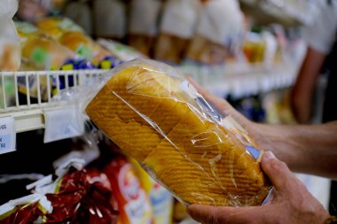 Erkek eli arka planda bulanık bir ekmek tutuyor, süpermarkette sebzeli raflar, pazarlama kavramı, tüketici mallarının fiyatları, bir tüketici sepeti.