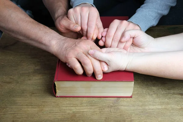 二人の男性と女性の手の近くに暗い赤いカバーの厚い家族の聖書の祈りのジェスチャーで折り畳まれた 永遠のキリスト教の価値観の概念 信仰の人々の団結 — ストック写真