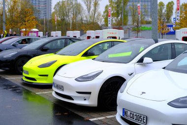 Frankfurt, Germany, October 2021: many Tesla light electric cars replenish battery at charging station, alternative energy development concept, electric vehicle production clipart