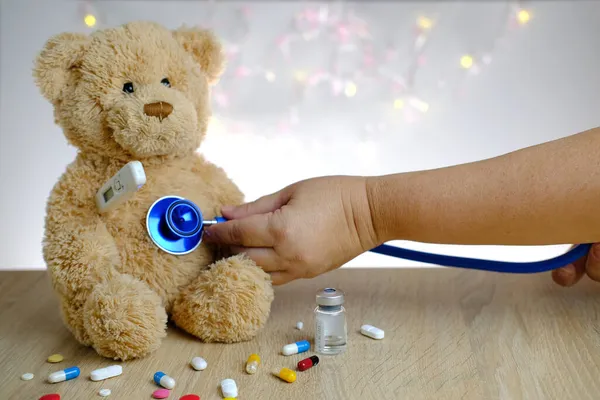 close-up of doctor's hand with stethoscope, many colored pills, medicine, capsules, teddy bear kids toy with stick thermometer, concept of pediatrics, childhood diseases, treatment