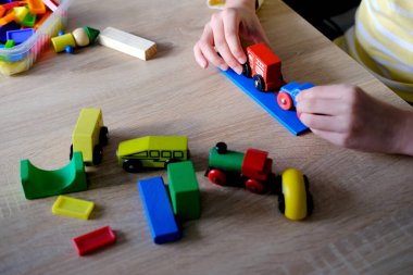 Çocukların ellerinde renkli tahta küpler, dominolar, çocuk 7-9 yaşları ev yapar, araba yuvarlar, inşaat konsepti, yaratıcılığın gelişimi, motor becerileri, sabır.