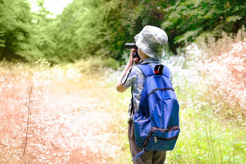 child of 7-8 years, boy in Panama hat, plaid shirt with walkie-talkie in hand stands in forest, looks carefully through binoculars, concept of hiking in nature, tourism, orienteering, survival in wild
