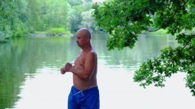Adam 60 yaşında, olgun yaşlarda, gölün kıyısında su kenarında spor yapıyor. Enerji kavramı her gün rutin sağlık uygulamaları. Erkek dayanıklılığı ve dayanıklılığı için iyi insan sağlığı.