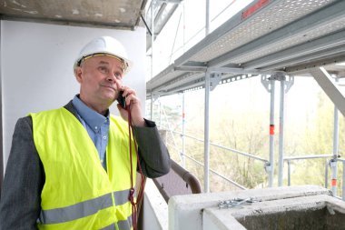 Tecrübeli bir inşaatçı, inşaat ekibi şefi, miğfer koruma mühendisi inşaat inşaatı için inşaat alanında telefonla konuşuyor, inşaat mühendisliği konsepti.