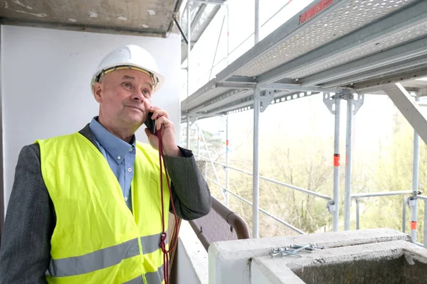 Tecrübeli bir inşaatçı, inşaat ekibi şefi, miğfer koruma mühendisi inşaat inşaatı için inşaat alanında telefonla konuşuyor, inşaat mühendisliği konsepti.