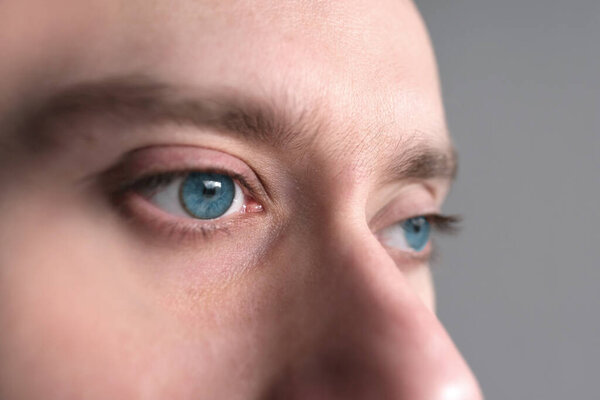 крупным планом часть мужского лица, парень, молодой голубоглазый мужчина 25-30 лет, человеческий глаз смотрит в сторону, концепция наблюдения, подглядывание, отслеживание, осмотр зрения, косметические процедуры, здоровье кожи