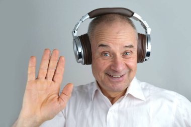 Olgun karizmatik bir adamın 60 yıl kulaklık takıp yüz hareketleriyle müzik dinlemesi, açık gri arka planda konsept öğrenmesi, yabancı dil öğrenmesi, canlı yayın ve vloglama