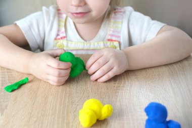 Küçük bir çocuğun, sarışın bir kızın ellerinde plastik oyuncaklar. 2 yaşında heykeller, renkli hamurdan karakterlerin figürleri. Güzel motor beceriler kavramı, dokunsal hisler, yaratıcılık.