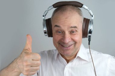 Olgun karizmatik bir adamın 60 yıl kulaklık takıp yüz hareketleriyle müzik dinlemesi, açık gri arka planda konsept öğrenmesi, yabancı dil öğrenmesi, canlı yayın ve vloglama