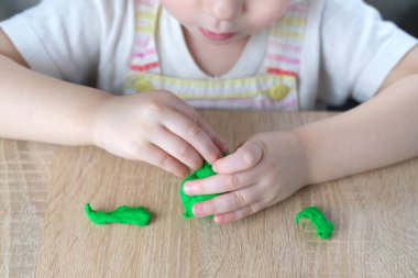 close-up plasticine toys in hands of toddler, small child, blonde girl 2 years old sculpts figures of characters from colored dough, concept of fine motor skills, tactile sensations, creativity clipart