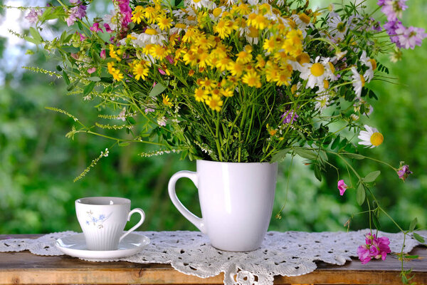 wooden table in the garden, tea, coffee in a mug, bouquet of wildflowers, concept of an outdoor tea party, good weather, a cozy summer mood