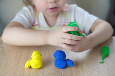 Küçük bir çocuğun, sarışın bir kızın ellerinde plastik oyuncaklar. 2 yaşında heykeller, renkli hamurdan karakterlerin figürleri. Güzel motor beceriler kavramı, dokunsal hisler, yaratıcılık.
